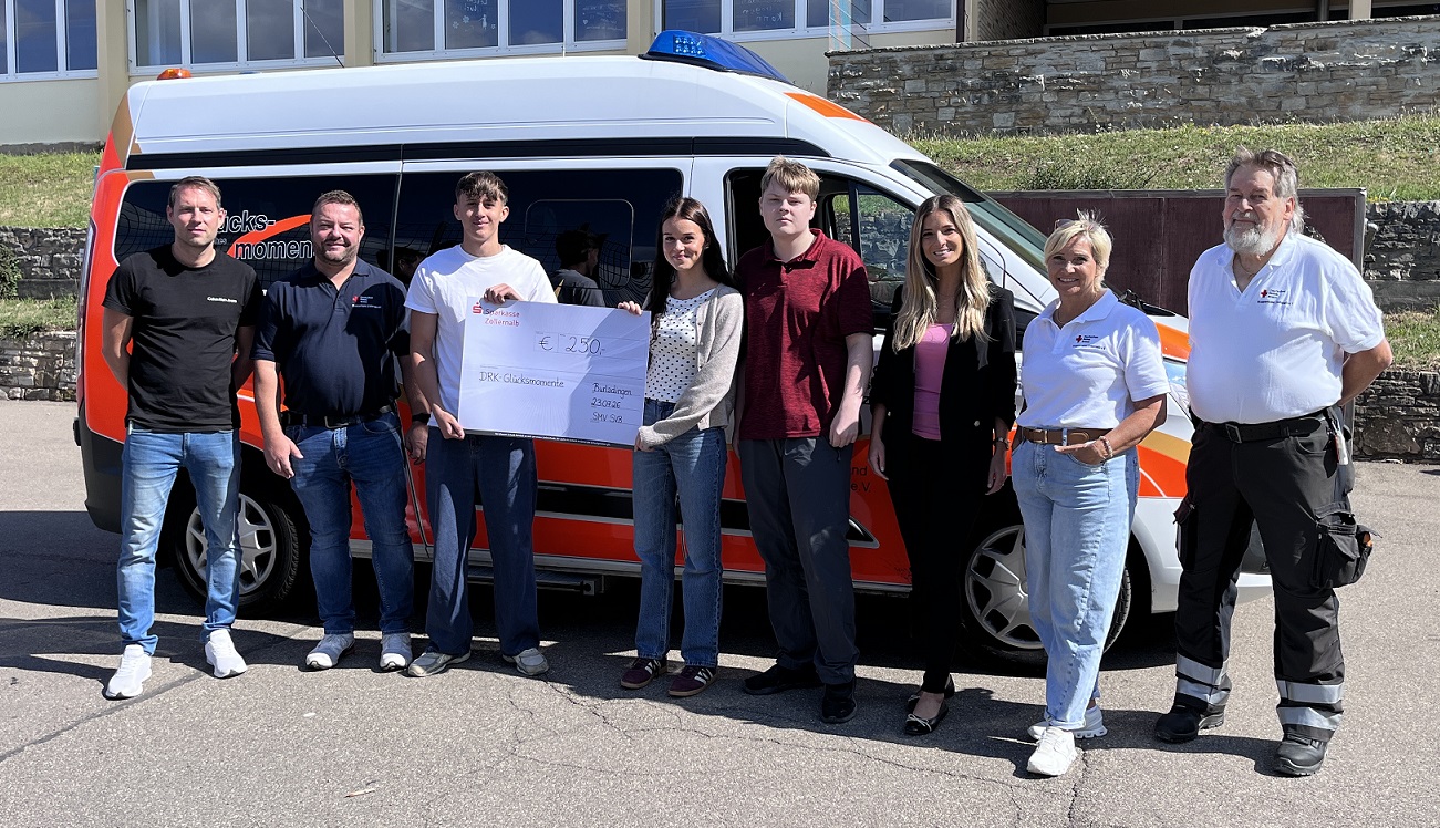 Das Bild zeigt 8 Personen vor einem Rettungswagen des DRKs. Eine Schülerin und ein Schüler halten einen großen Scheck (250 Euro) in der Hand. Ein weiterer Schüler steht direkt daneben. Außerdem befinden sich auf dem Bild: 1 Mitarbeiterin und 2 Mitarbeiter des DRKs sowie Fr. Arutjunova und Hr. Schroft vom Schulverbund Burladingen.  